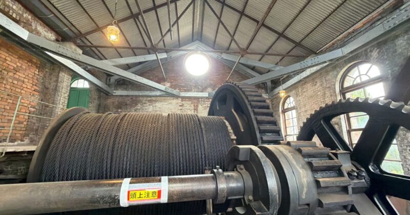 万田坑の第二竪坑巻上機。巨大な鉄製ドラムに太いワイヤーが巻かれ、レンガ造りの機械室内に設置されている様子。